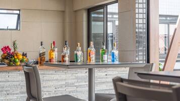 Zona de bar con mostrador que exhibe varias botellas, un frutero y dos sillas.