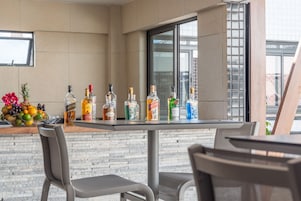 Zona de bar con mostrador que exhibe varias botellas, un frutero y dos sillas.