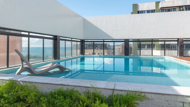 A rooftop swimming pool with clear blue water, surrounded by large windows offering views of the cityscape. - Palms Ponta Verde by Tropicalis (Maceió)