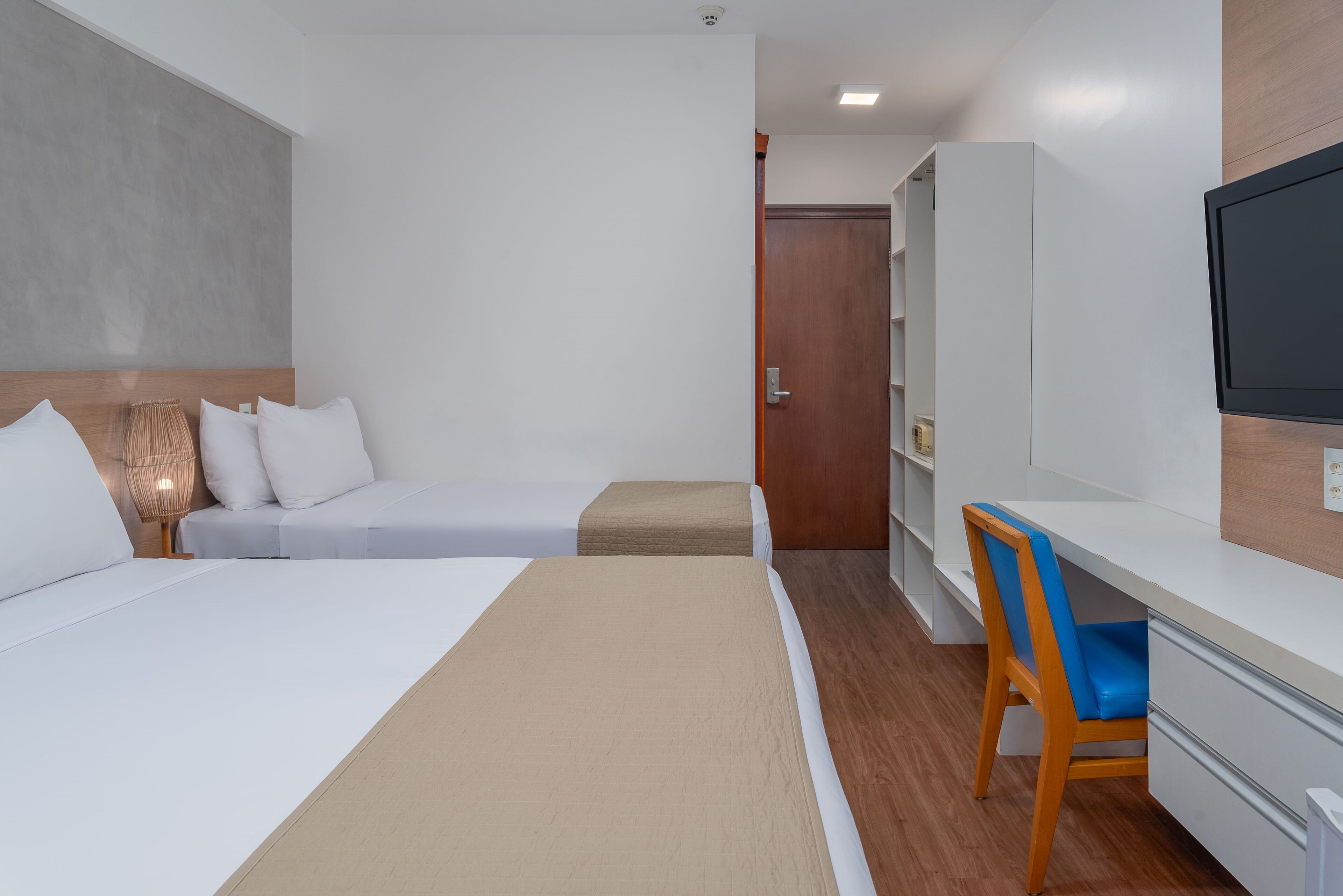 A hotel room with a bed, a desk, a chair, a television, and a wardrobe.