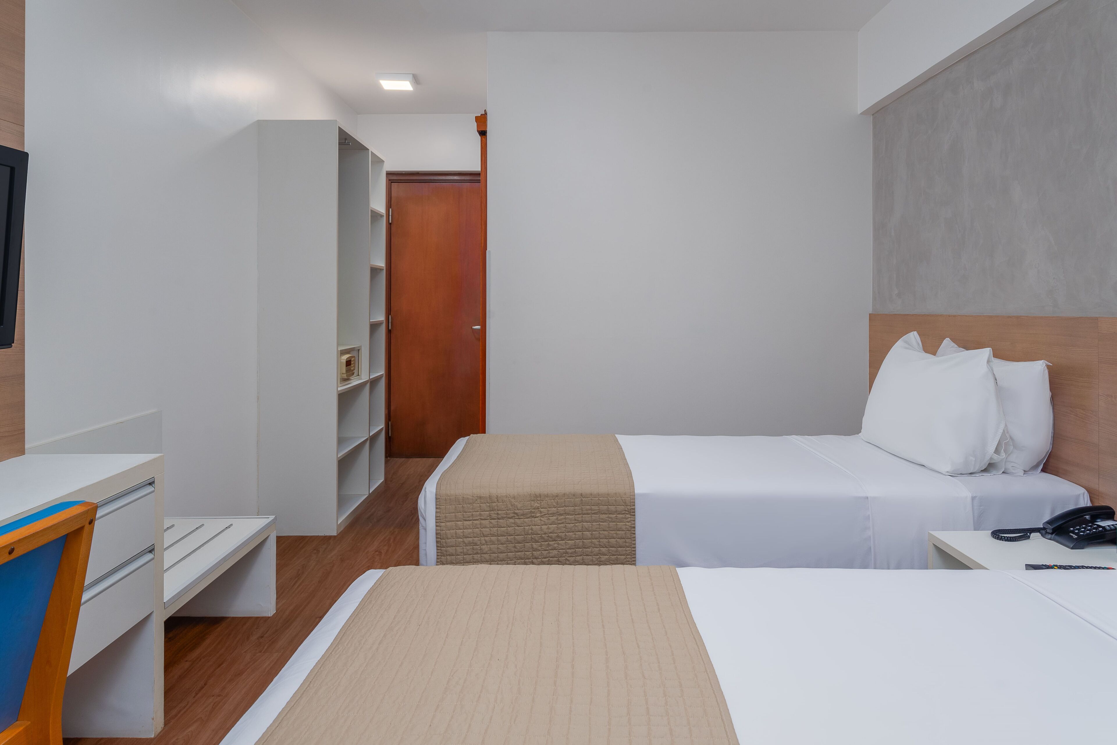 Una camera d'albergo con due letti, una scrivania, un armadio e un telefono.