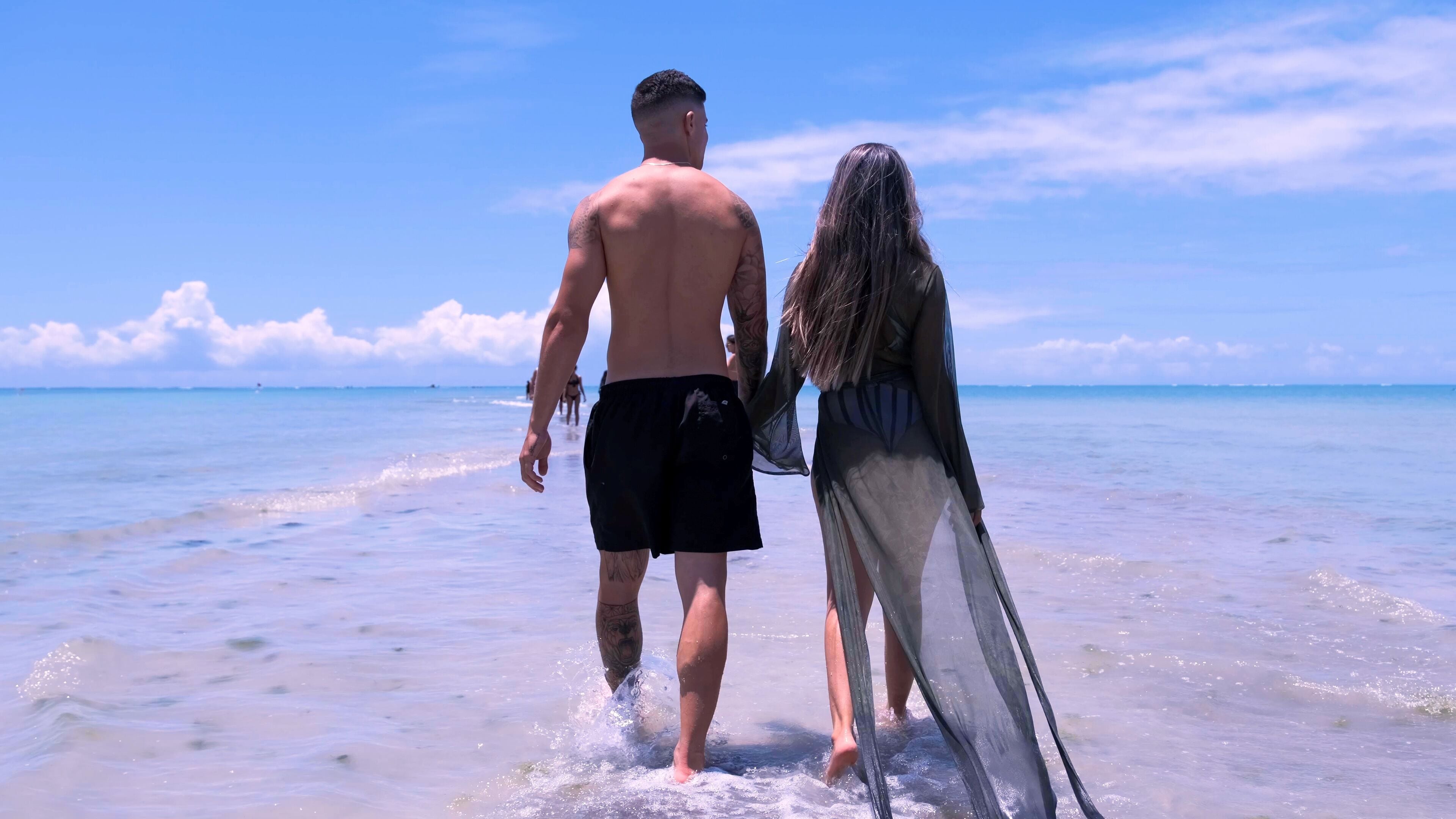 Dos personas caminando en una playa con cielo despejado y mar tranquilo.