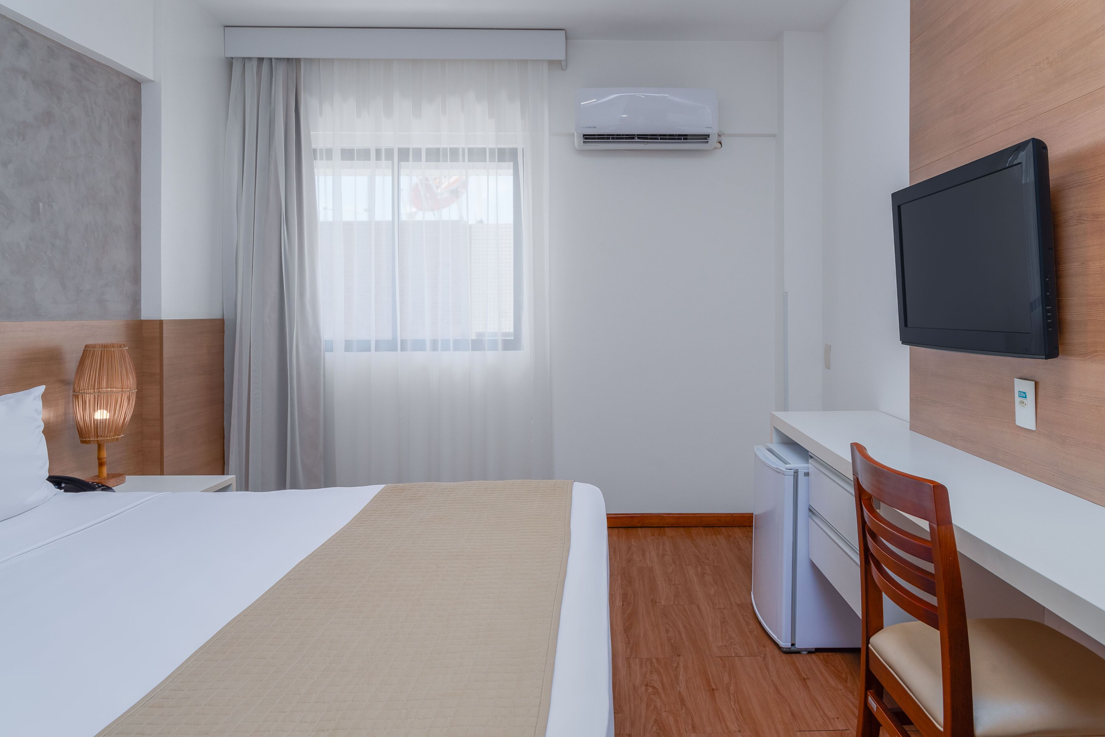 Una habitación de hotel con una cama, un escritorio, una silla, aire acondicionado y televisión.