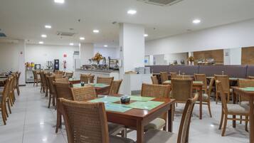 Un comedor amplio con varias mesas y sillas, una zona de cocina al fondo, y un ambiente limpio y bien iluminado.