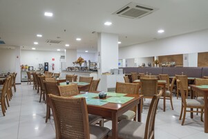 Un comedor amplio con varias mesas y sillas, una zona de cocina al fondo, y un ambiente limpio y bien iluminado.