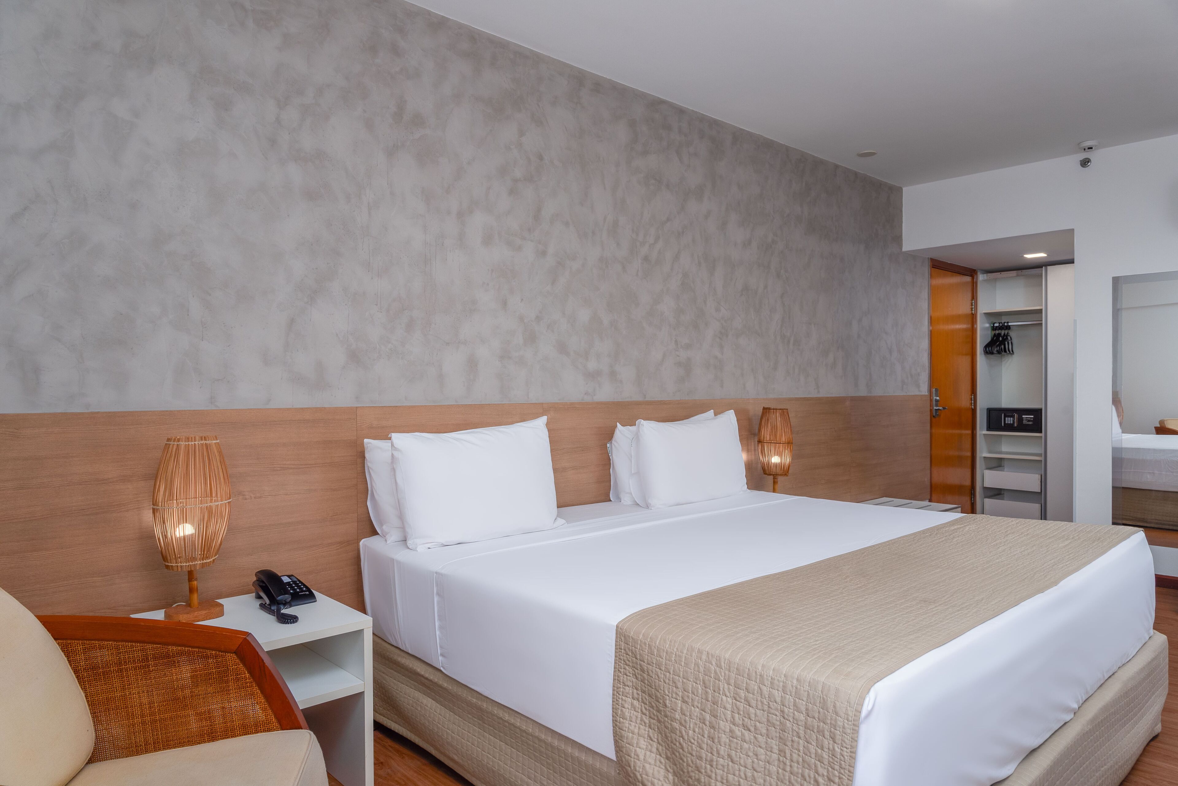 Una habitación de hotel con una cama grande, una mesita de noche con lámpara, una silla y un armario.