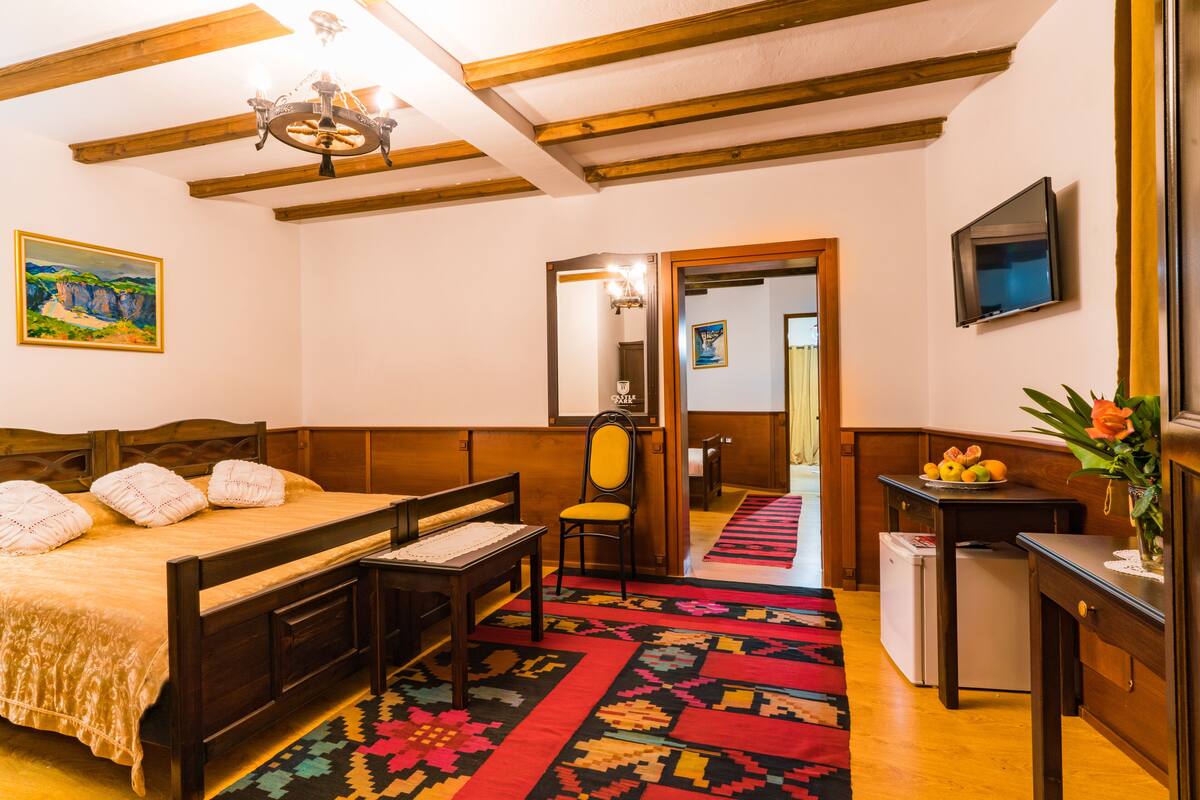A bedroom with a wooden bed, a small desk, a chair, a television, and a refrigerator.
