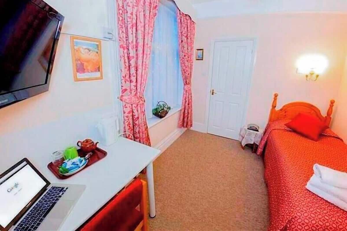 A bedroom with a bed, a desk with a laptop, a TV, and a window with curtains.