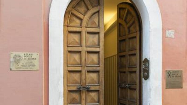 An arched doorway with a wooden door, a plaque on the wall, and a tiled floor. - Relais Bocca di Leone (Rome)