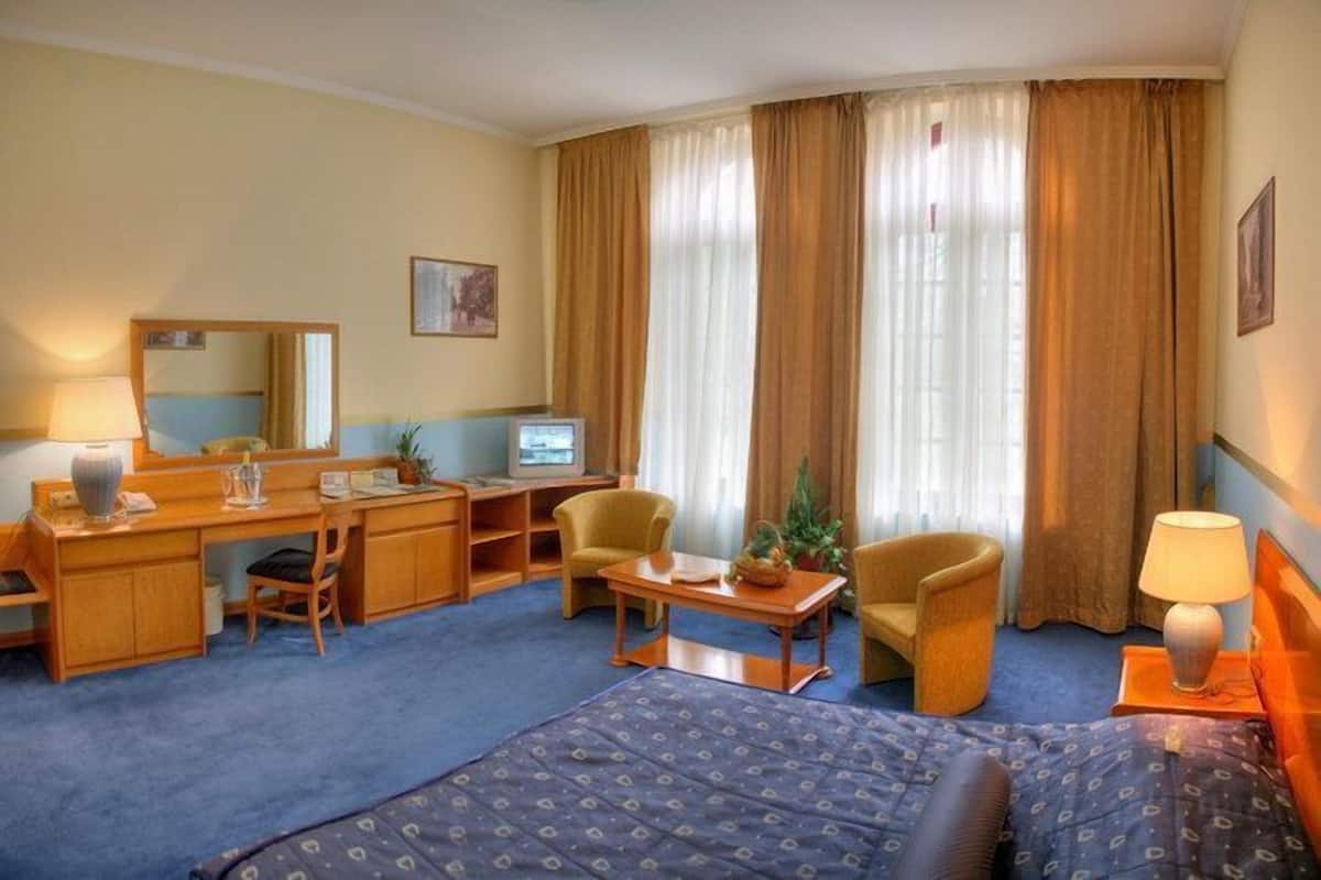 Quarto de hotel com cama, escrivaninha, cadeira e televisão.