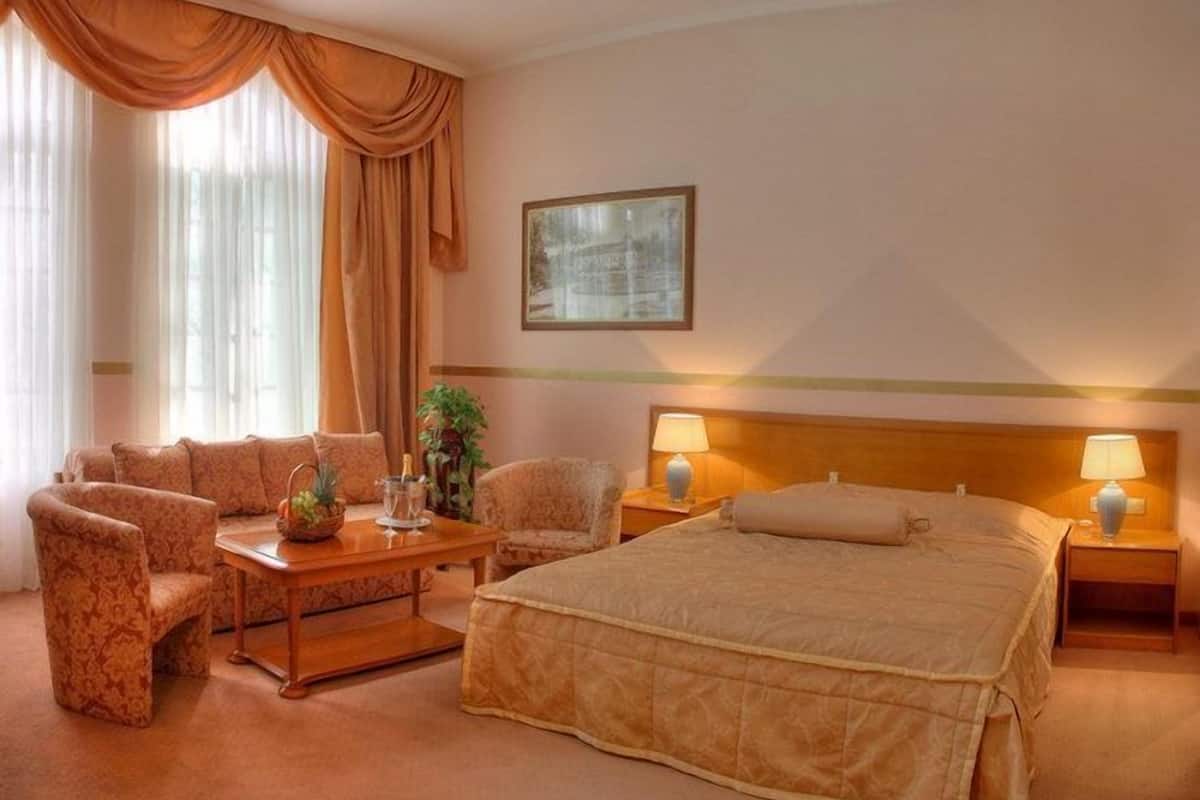 Quarto de hotel com uma cama, duas mesas de cabeceira com abajures, um sofá e uma mesa de centro.