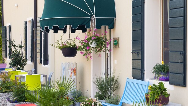An outdoor seating area with a green umbrella, potted plants, and a blue chair.