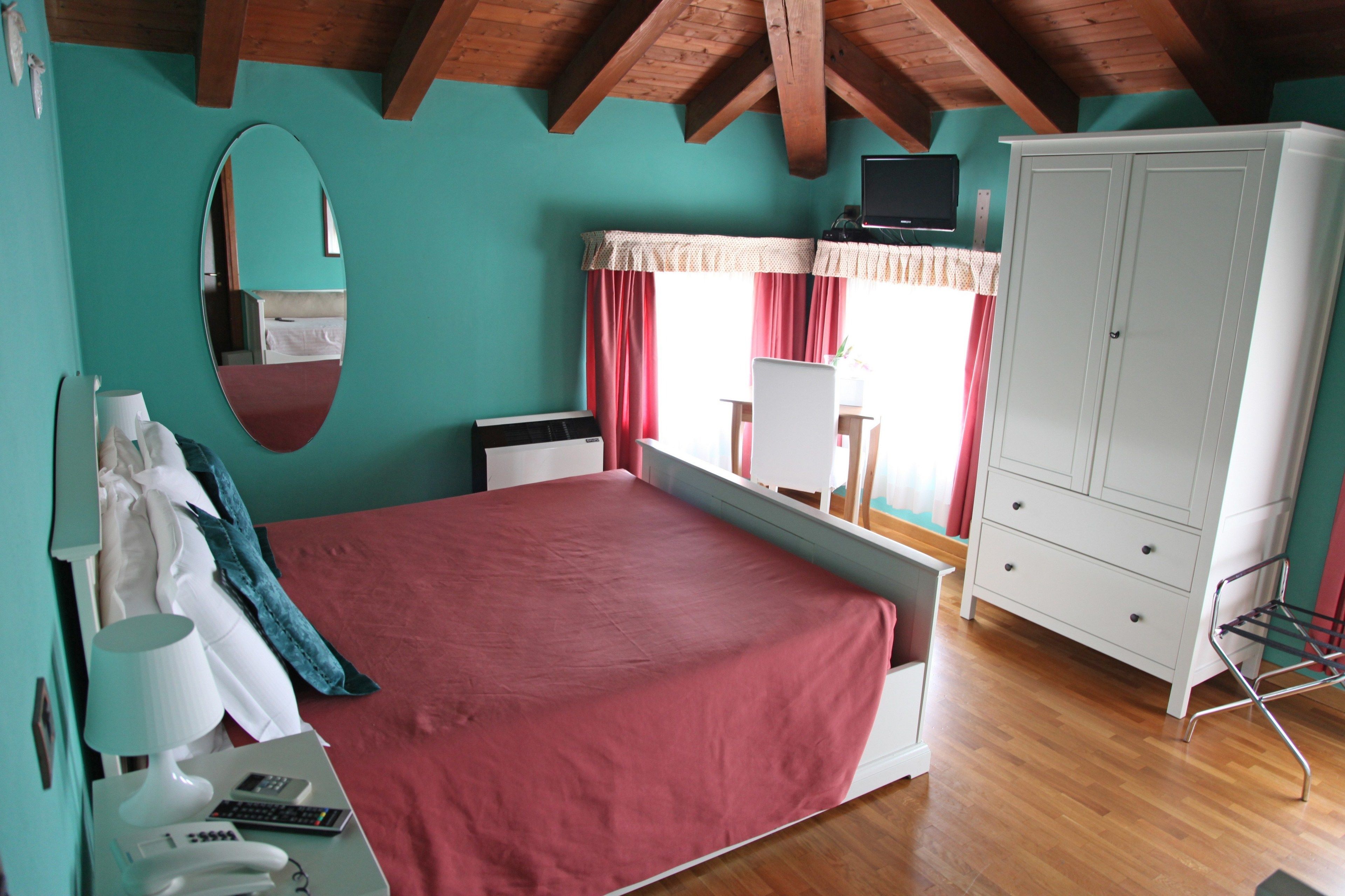 A bedroom with a bed, a desk, a wardrobe, a mirror, and a television.