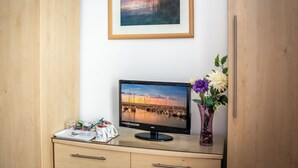 A room with a wooden desk, a monitor displaying a marina scene, a framed picture above the desk, and a vase with flowers to the right. - The Richmond Bed & Breakfast (Shanklin)