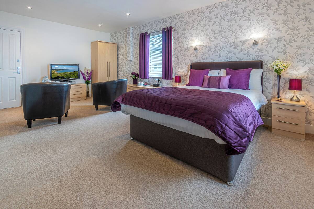 A bedroom with a large bed, a television, a desk, and a wardrobe.