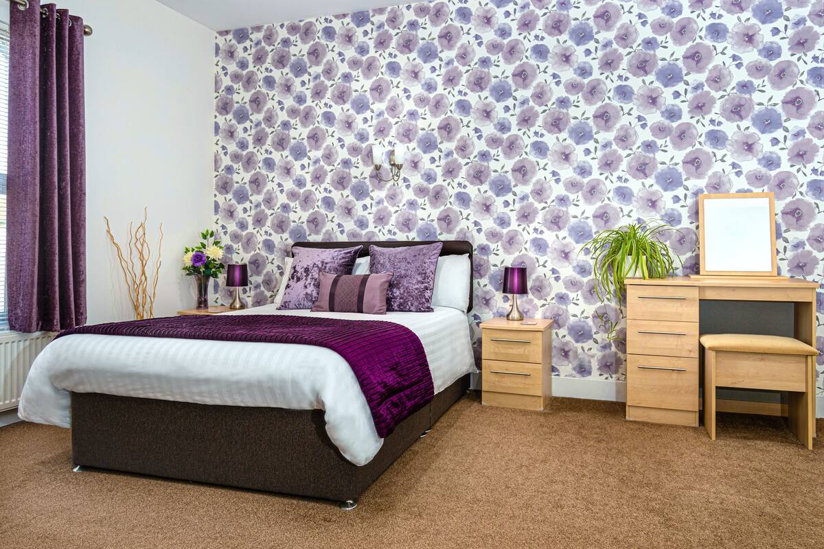 A bedroom with a bed, nightstands, a desk, and a chair.