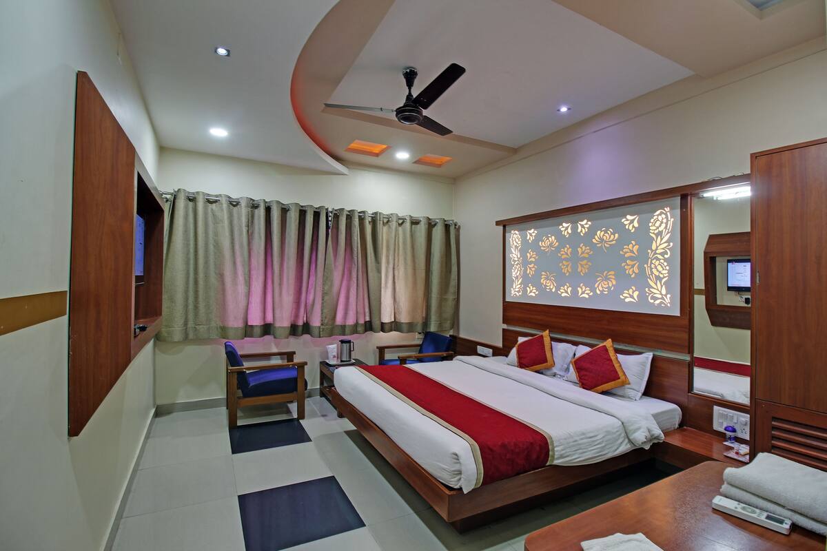 Una habitación de hotel con cama, mesita de noche, silla, cortinas y un ventilador de techo.