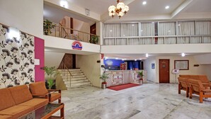 A hotel lobby with a reception desk, seating area, staircase, and a view of the upper floor. - Hotel Sunset Inn Mount Abu with Swimming Pool (Abu Road)