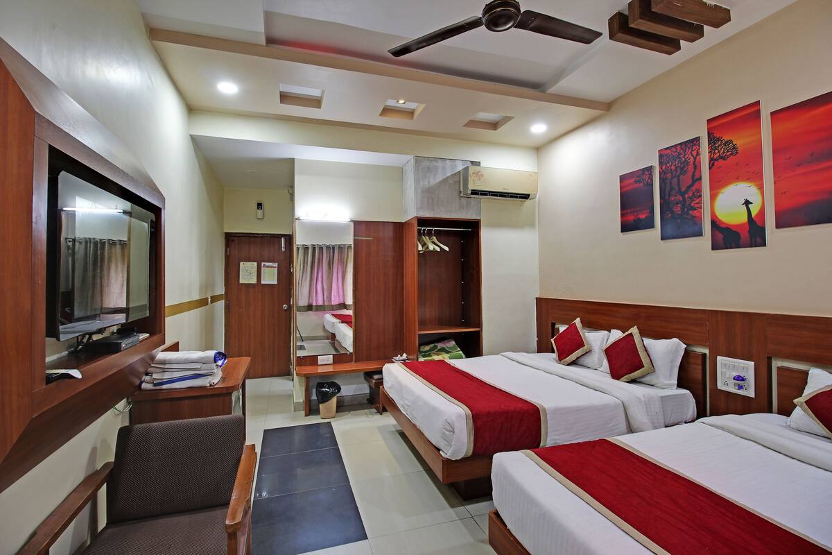 Habitación de hotel con dos camas, televisión, escritorio y armario.