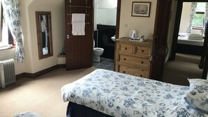 A bedroom with a bed, a dresser, a radiator, a bathroom visible through an open door, and a window with curtains. - Balloan House (Muir of Ord)