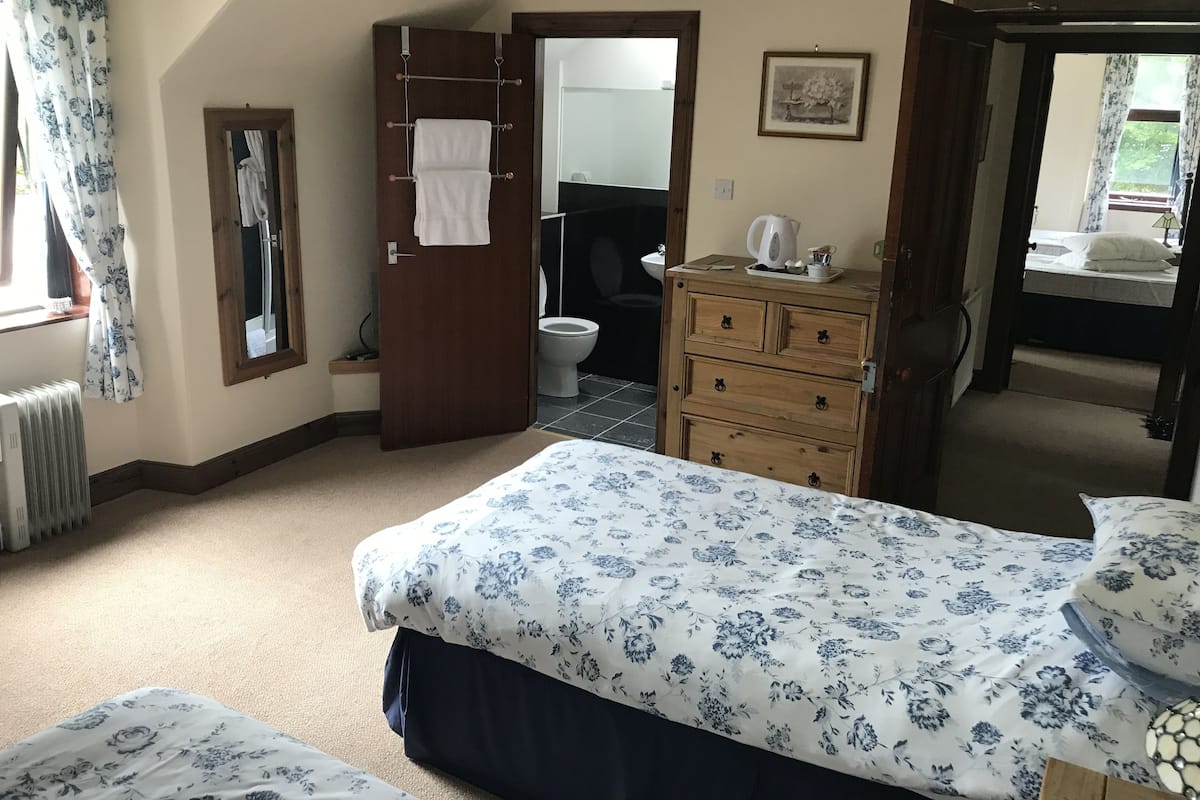 A bedroom with a bed, a dresser, a radiator, a bathroom visible through an open door, and a window with curtains.