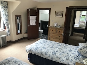 A bedroom with a bed, a dresser, a radiator, a bathroom visible through an open door, and a window with curtains. - Balloan House (Muir of Ord)