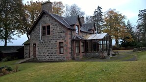 A stone house with a sloped roof and a glass conservatory. - Balloan House (Muir of Ord)