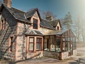 A stone house with a gabled roof, a covered porch, and a chimney. - Balloan House (Muir of Ord)