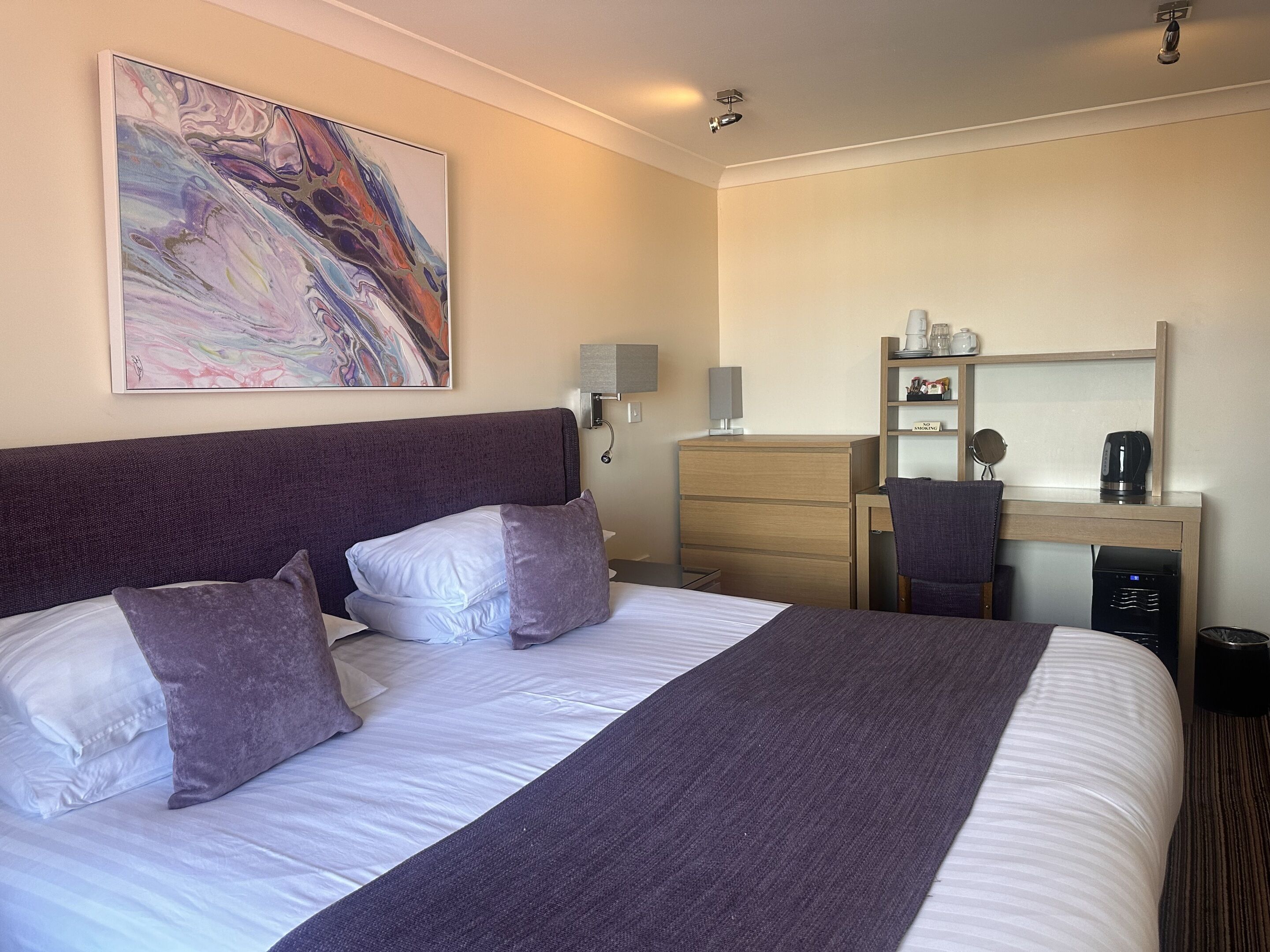 A hotel room with a large bed, a dresser, a desk with a mirror, and a coffee maker.