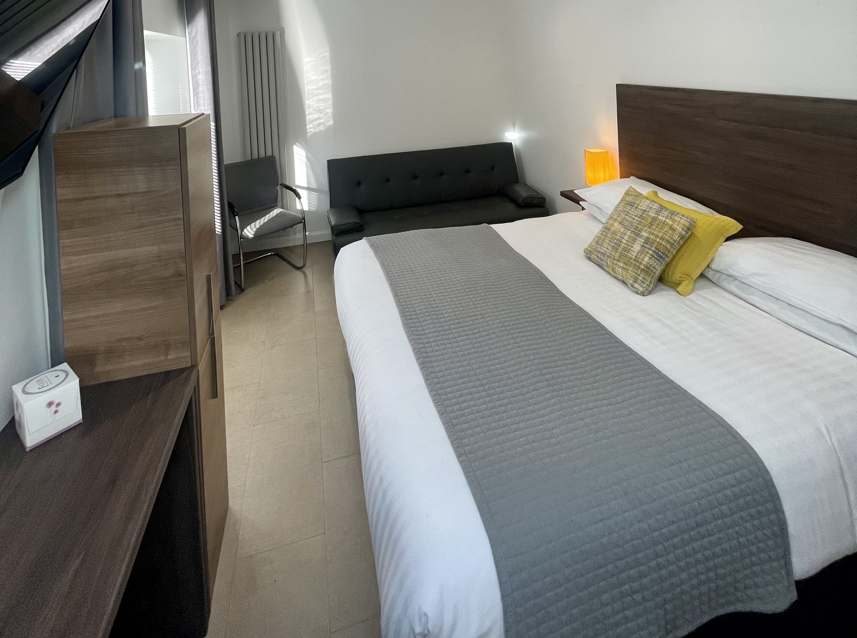 A hotel room with a bed, bedside table, chair, and a lamp.