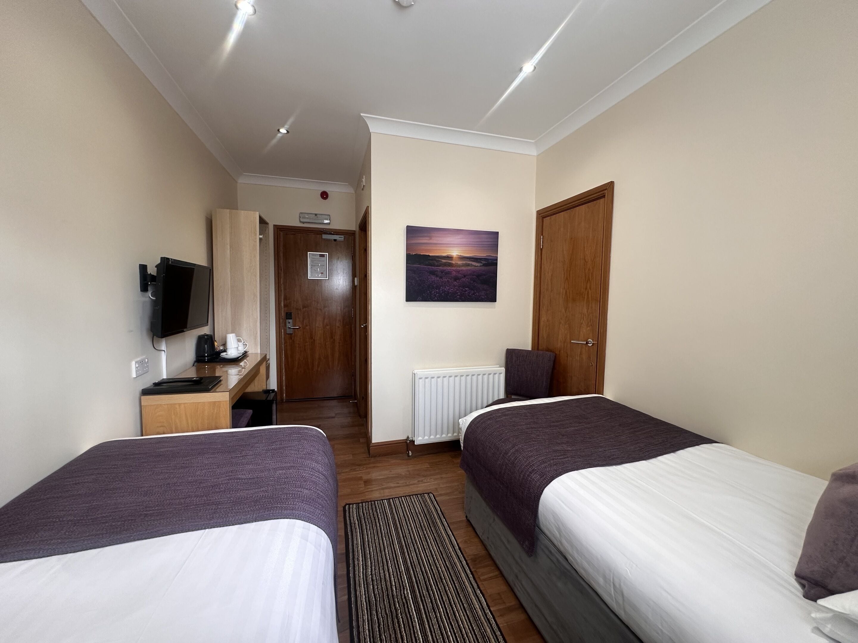 Ein Hotelzimmer mit zwei Betten, einem Schreibtisch mit Computer, einem Fernseher und einem Bild an der Wand.