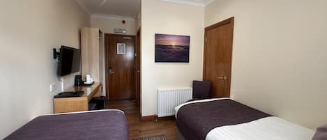 Ein Hotelzimmer mit zwei Betten, einem Schreibtisch mit Computer, einem Fernseher und einem Bild an der Wand.