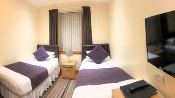 A hotel room with two beds, a TV, a bedside table, and a window with curtains.