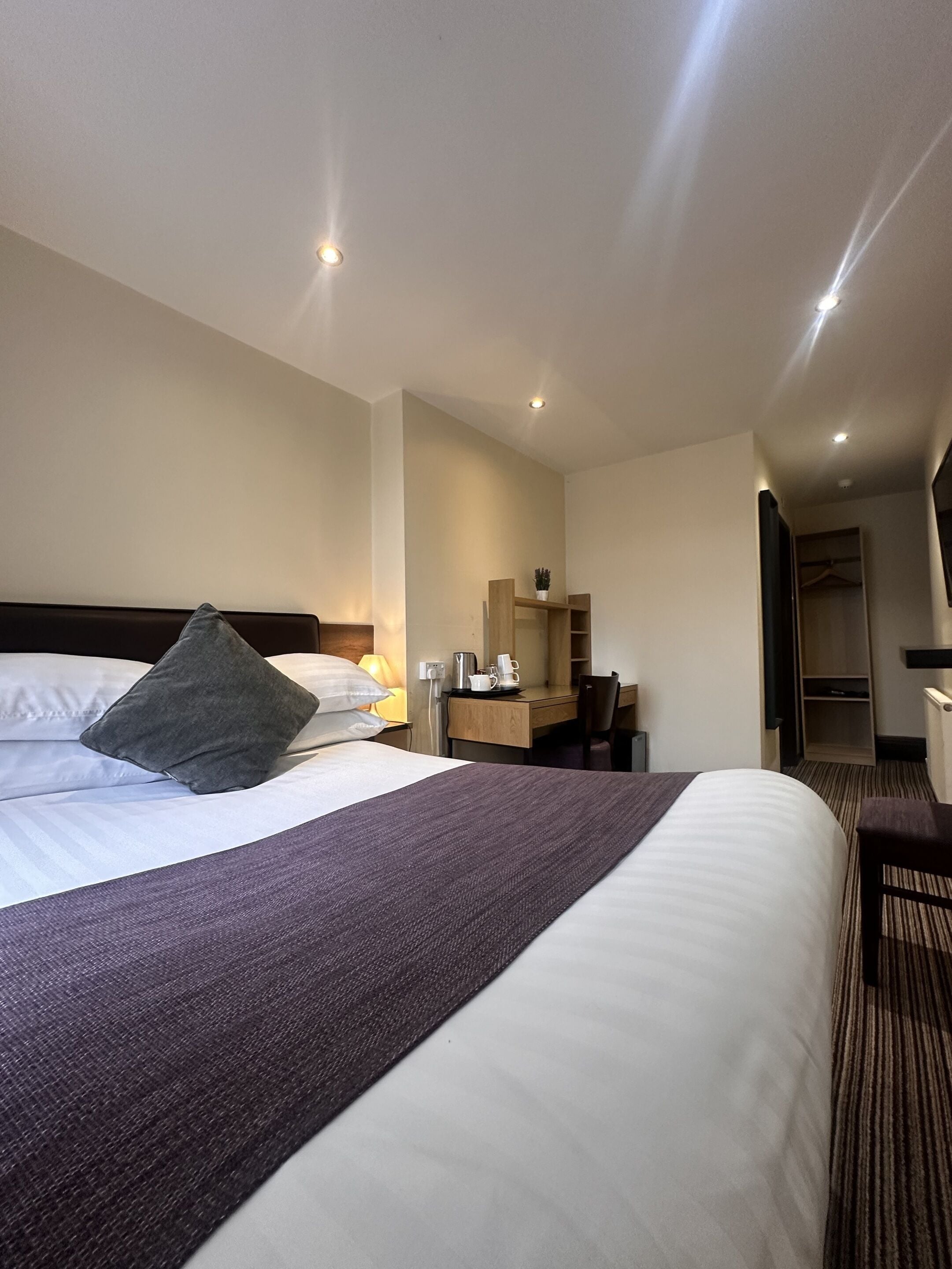 Una habitación de hotel con una cama grande, un escritorio con una silla, un armario y un espejo.