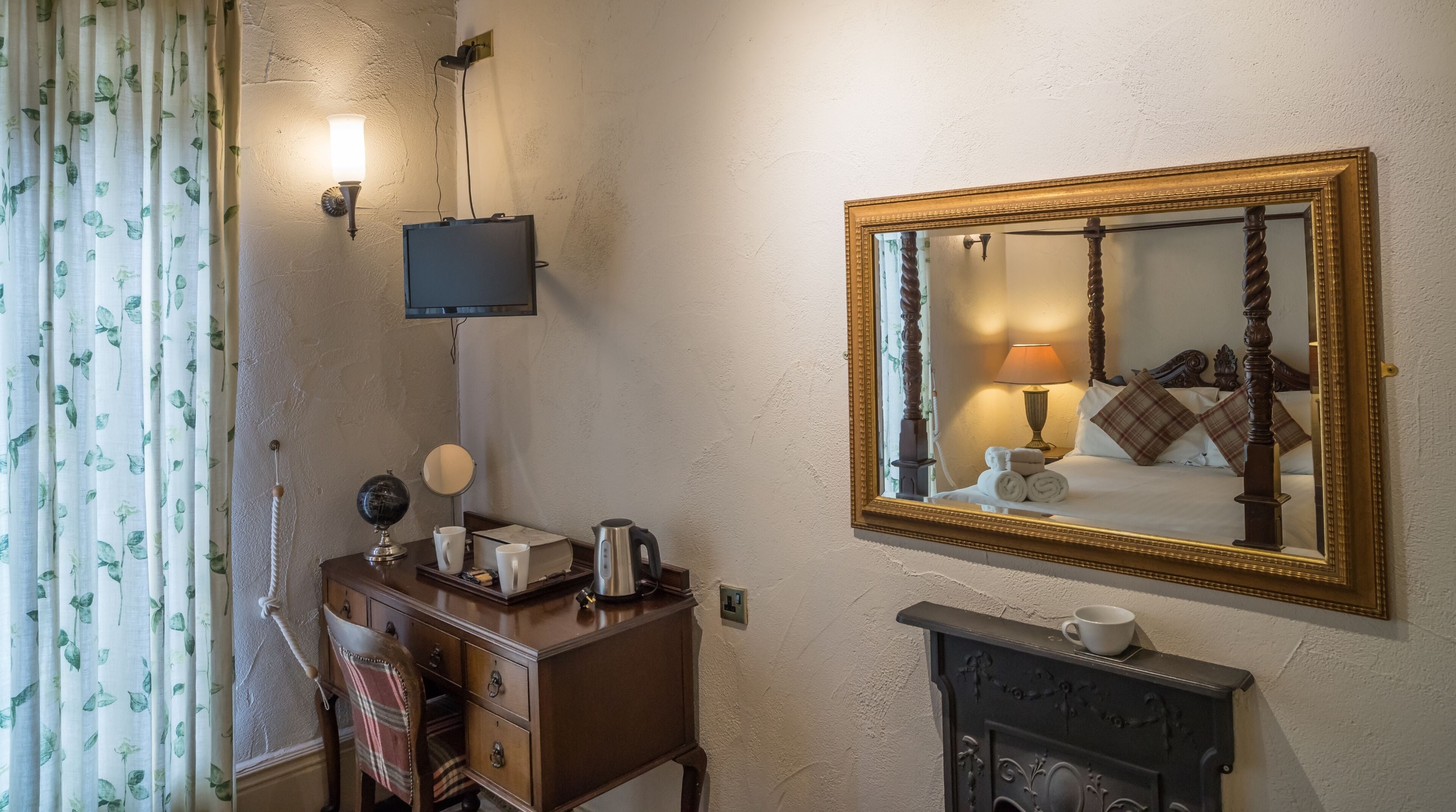 Habitación de hotel con cómoda de madera, un globo terráqueo, espejo, cama con cabecera, lámpara y chimenea.