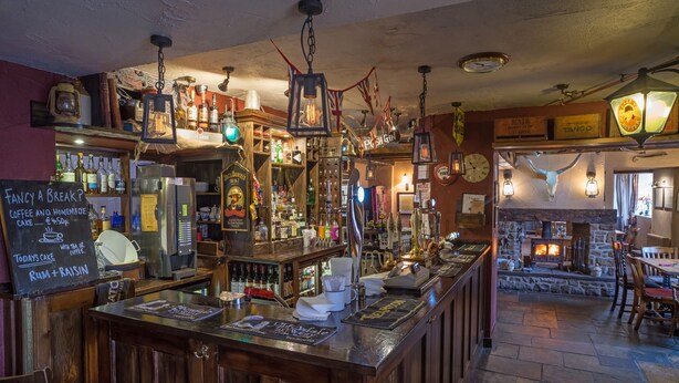 A bar area with wooden bar counters, hanging lanterns, and a fireplace. - The Peak Hotel (Hope Valley)
