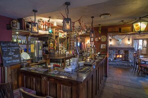 A bar area with wooden bar counters, hanging lanterns, and a fireplace. - The Peak Hotel (Hope Valley)