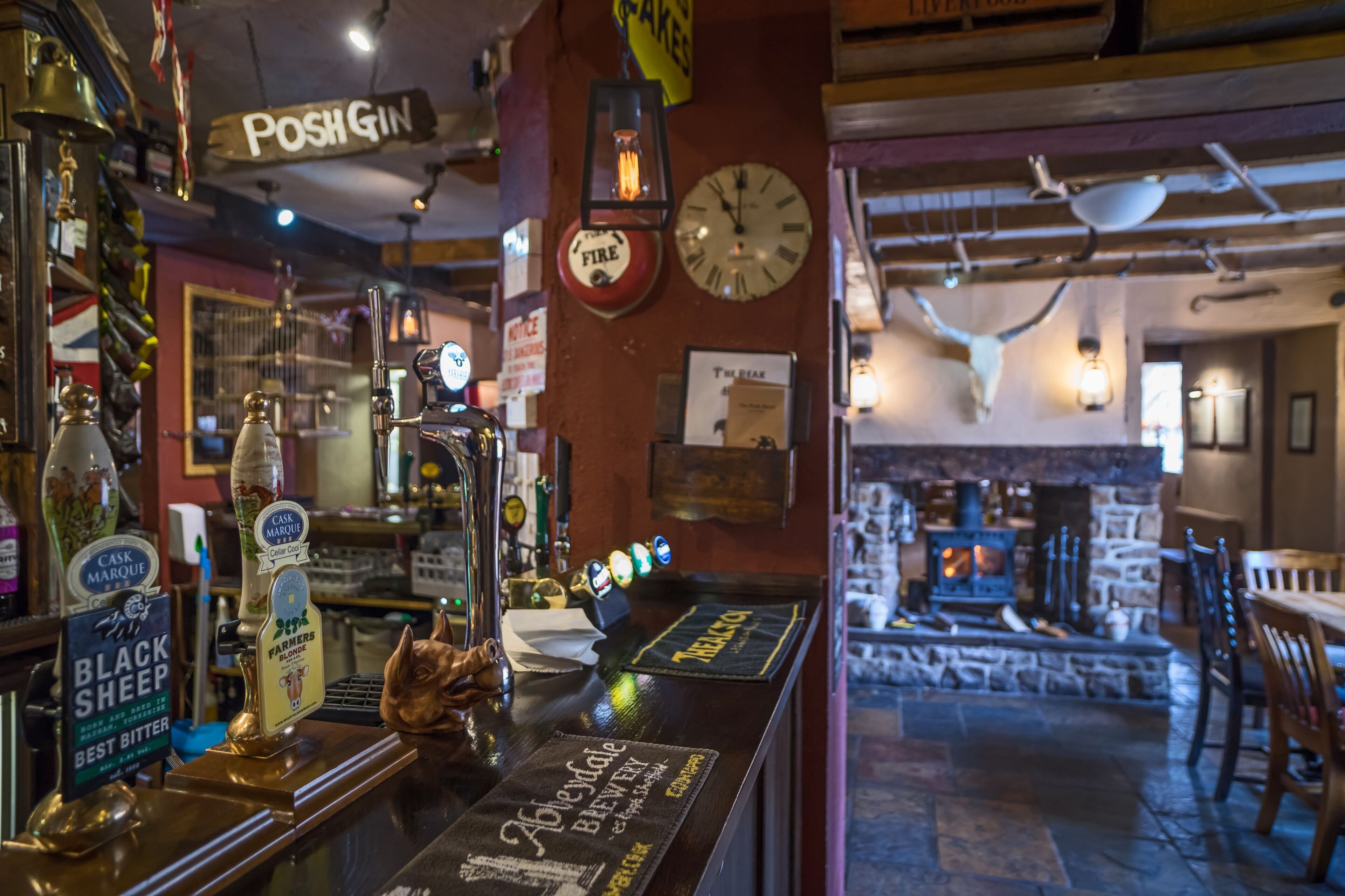 A bar area with a wooden counter, beer taps, and a fireplace in the background.