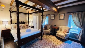 A four-poster bed with a matching canopy, a large patterned rug, and a seating area with two armchairs and a small table. - The Peak Hotel (Hope Valley)