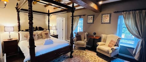 A four-poster bed with a matching canopy, a large patterned rug, and a seating area with two armchairs and a small table.
