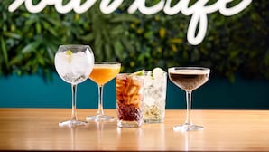 Four different cocktails on a wooden table with a bar sign in the background. - Travelodge Cardiff Central Queen Street (Cardiff)