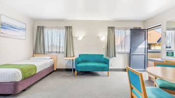 A hotel room with a bed, a teal armchair, a small table, and a window with curtains.