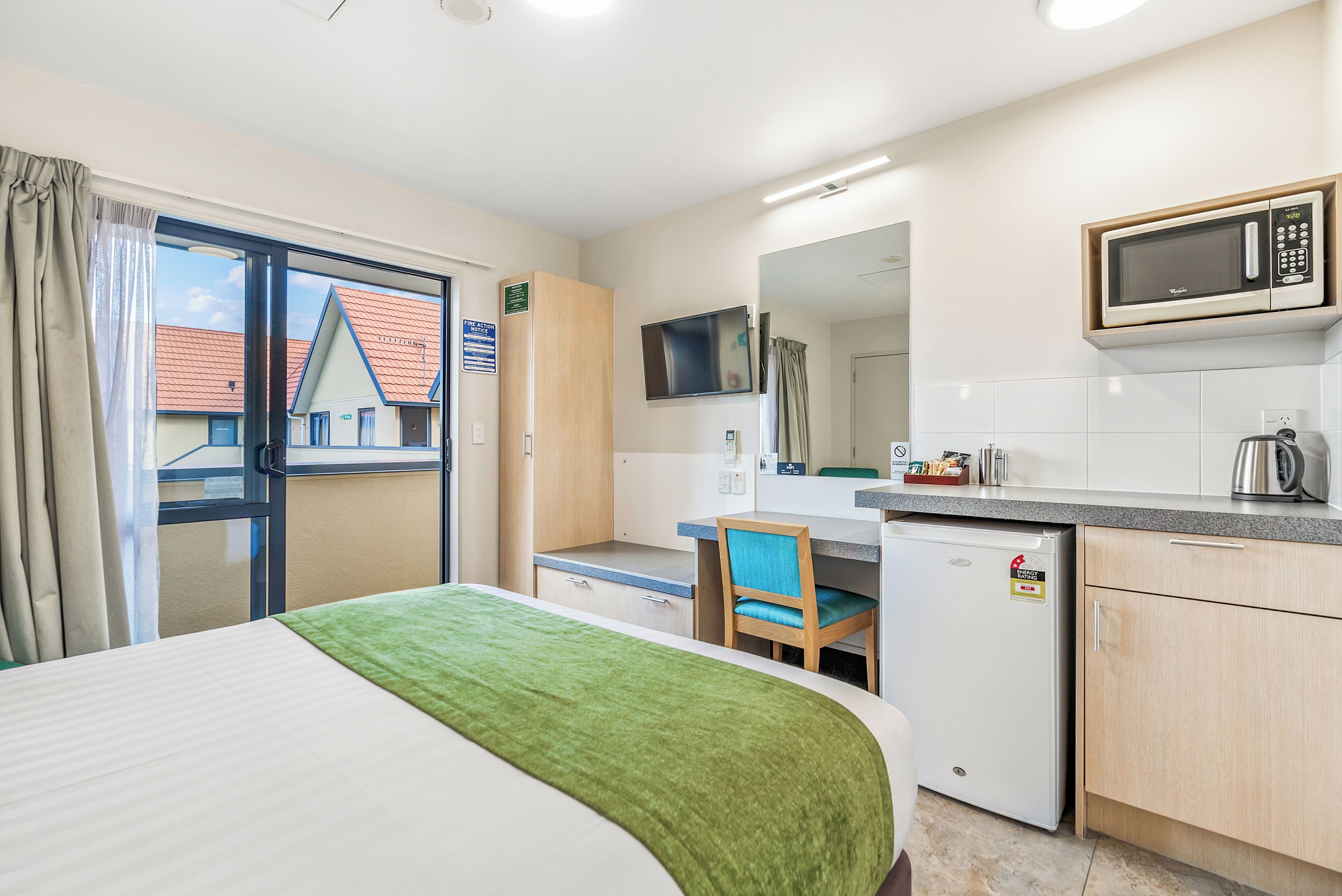 A hotel room with a bed, a desk, a chair, a microwave, a small refrigerator, and a window with curtains.