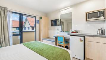 A hotel room with a bed, a desk, a chair, a microwave, a small refrigerator, and a window with curtains.