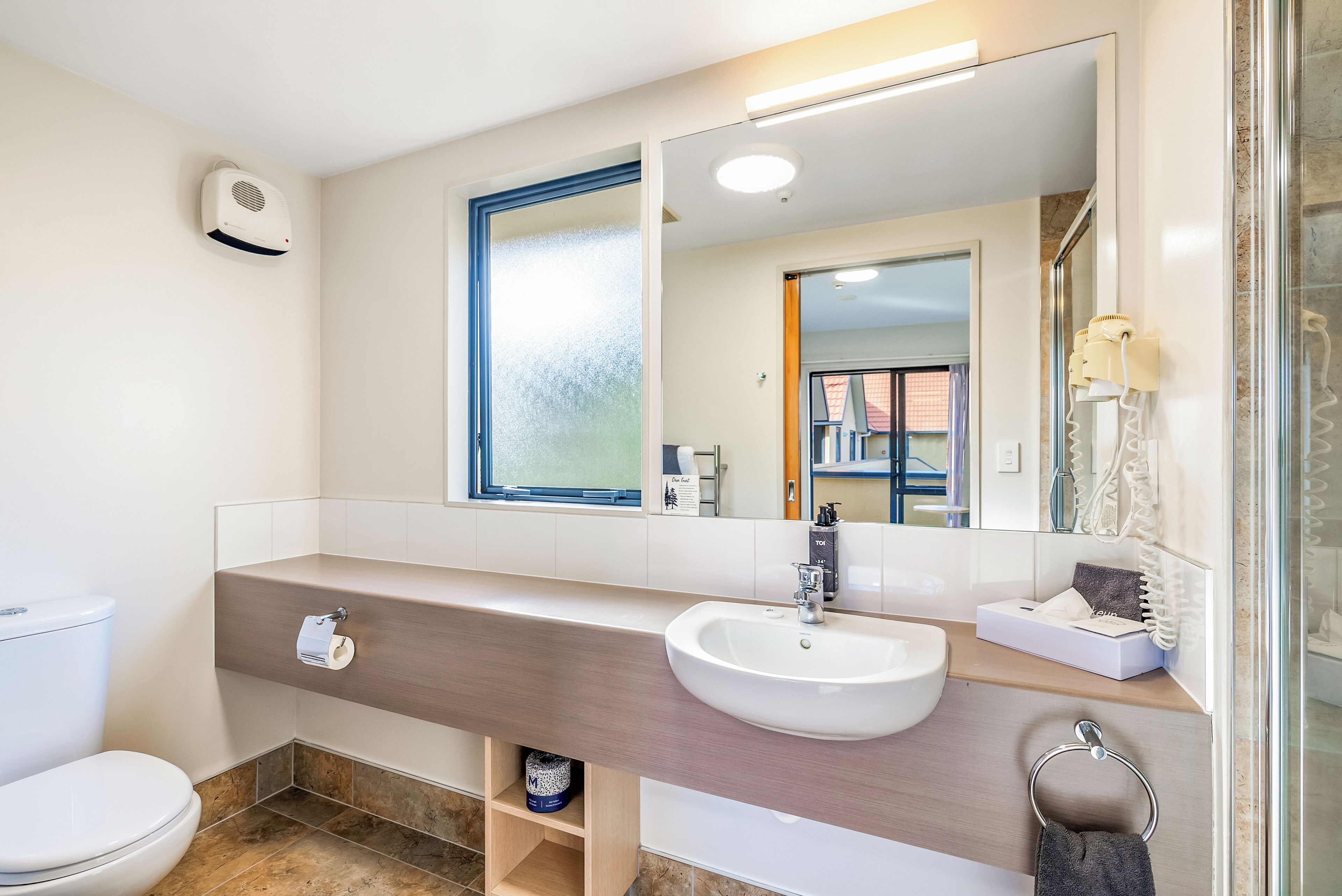 A bathroom with a toilet, sink, mirror, and shower area.