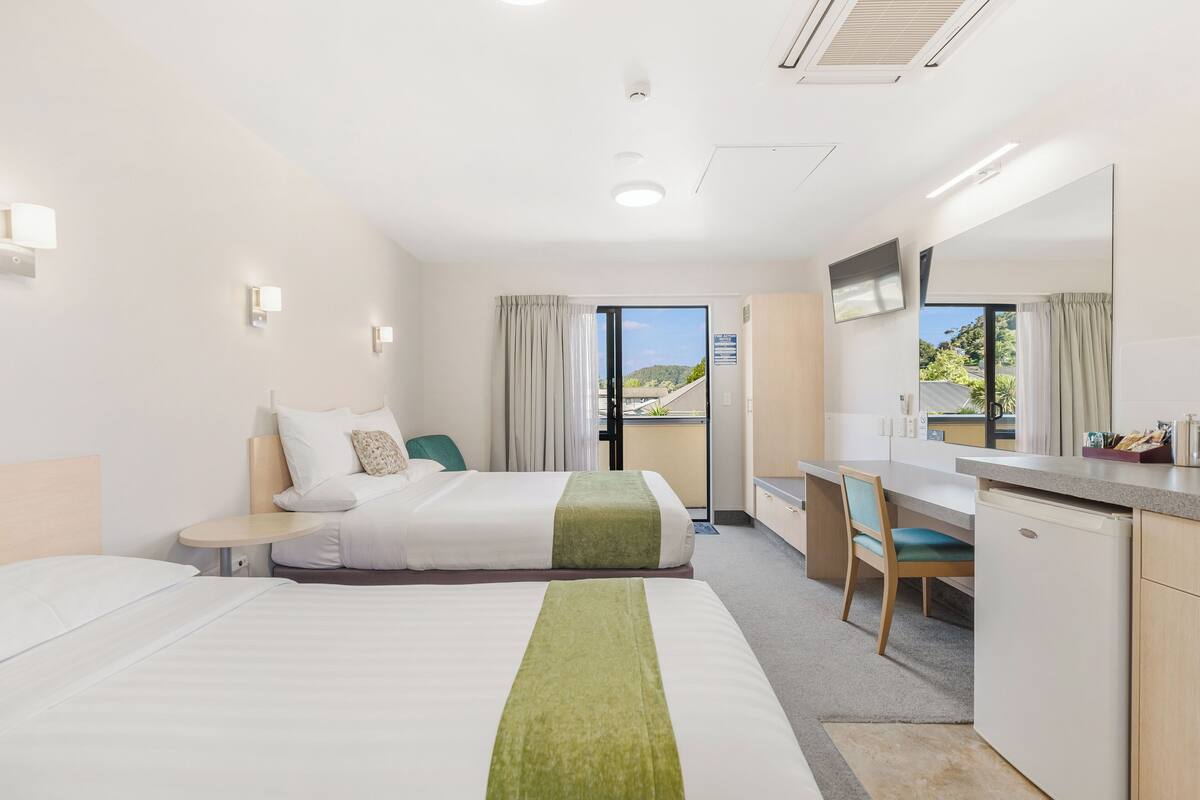 Habitación de hotel con cama, escritorio, silla, mesita, espejo y vistas al exterior.