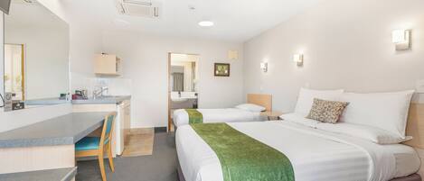 A hotel room with a desk, two beds, a bathroom, and a hallway.