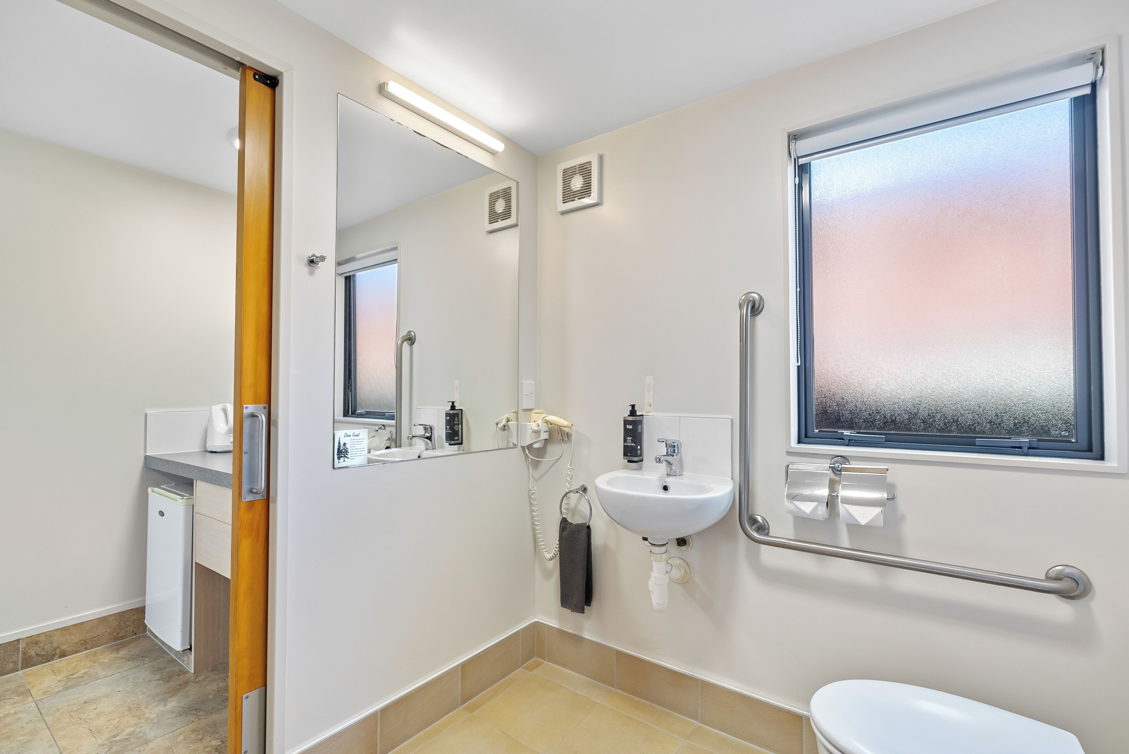A modern bathroom with a toilet, sink, mirror, and a window.
