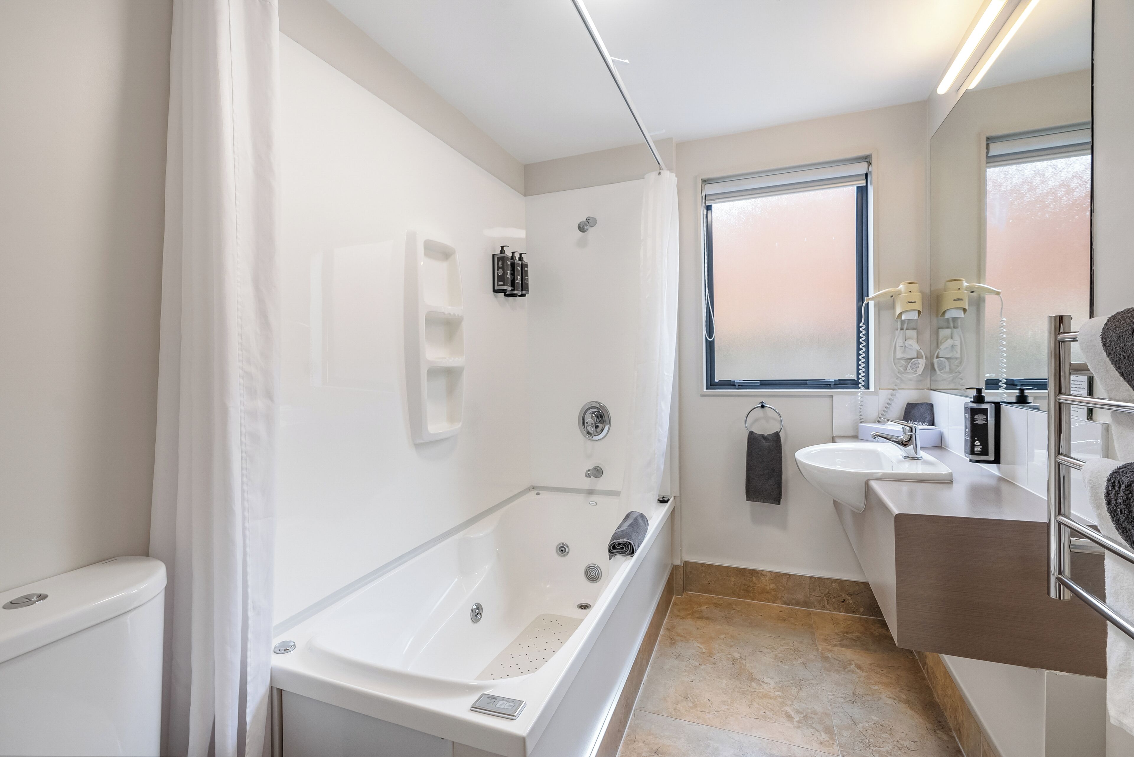 Een moderne badkamer met een bad, douche, wastafel en een raam.