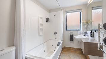 Een moderne badkamer met een bad, douche, wastafel en een raam.